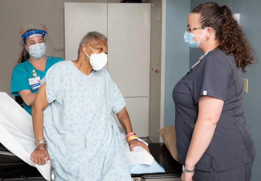 Two providers help a patient onto a table for radiation therapy