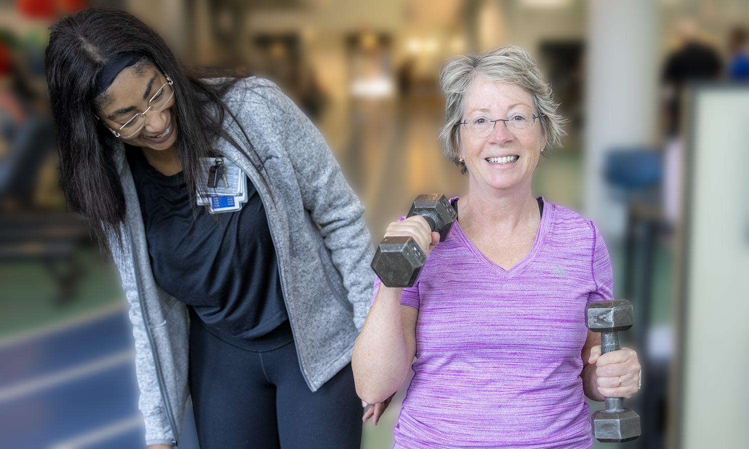 A trainer watches a client lift dumbbells 