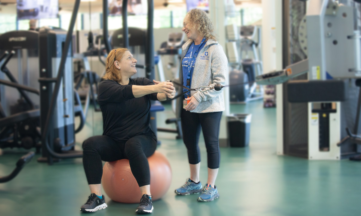 A trainer helps a client with an exercise on a balance ball