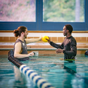 Un especialista en fisioterapia pasa una pelota con un paciente en una piscina