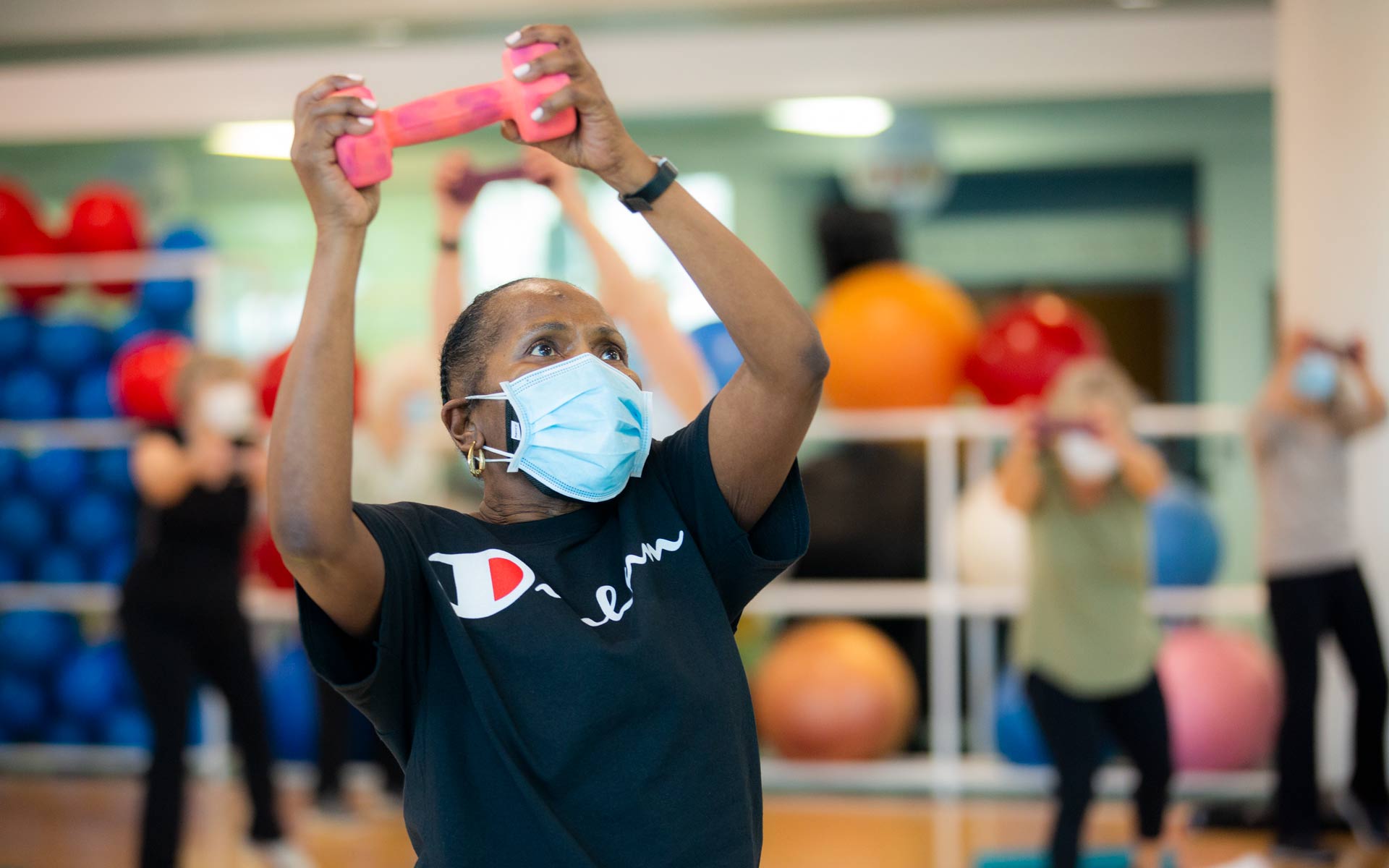 A woman lifts a weight over her head during a group exercise class