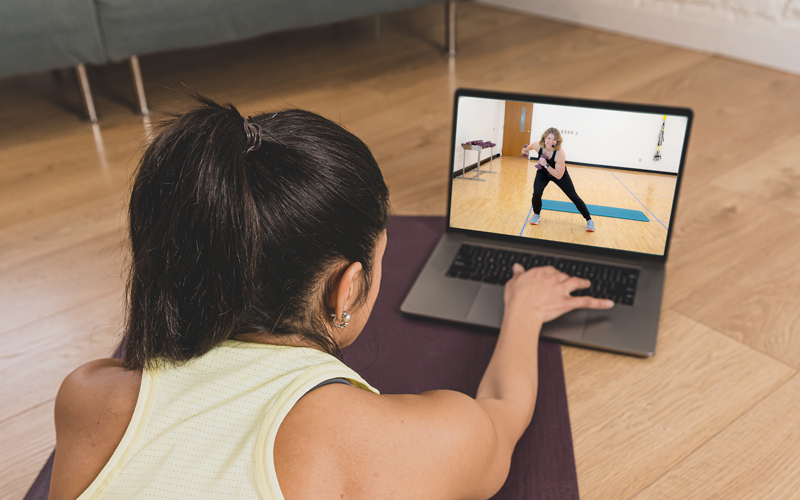 A woman joins an online fitness class on her laptop