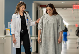 A physician helps a patient walk down a hallway