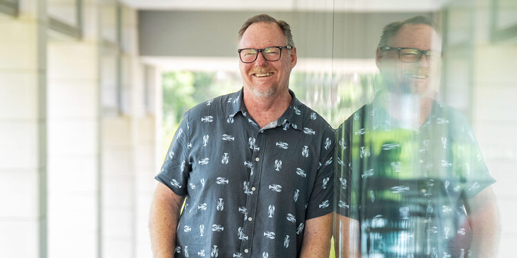 Brad Dugai leans against the glass wall of a building