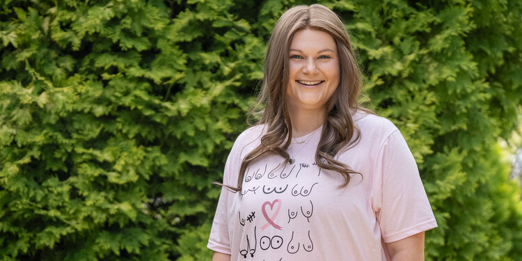 Bailey Geason smiles outside. She is wearing a breast cancer survivor shirt with icons of breasts on it.