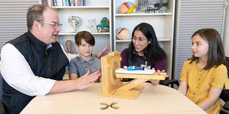 A provider shows a small model of an MRI to two kids and their dad