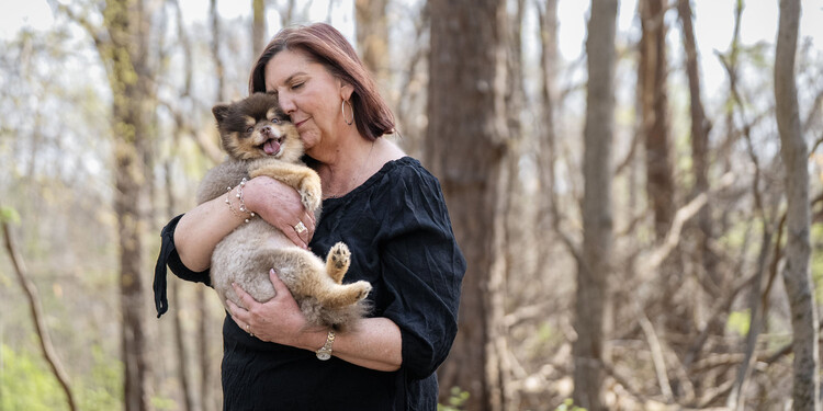 Juli stands on a forest trail and cuddles her dog Boba against her face