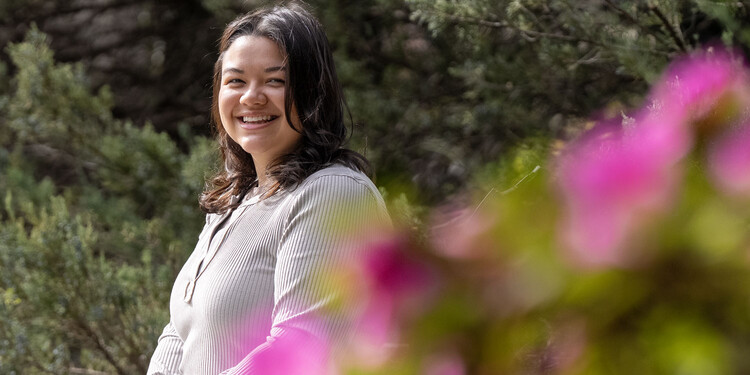 Marisa Chow se sienta en un banco frente a unas flores rosadas
