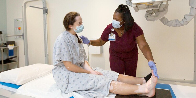 A provider helps a patient prepare for an X-Ray of their foot and ankle.
