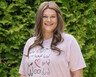 Bailey Geason sonríe afuera. Lleva una camiseta de sobreviviente de cáncer de mama con íconos de pechos.