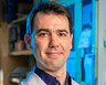 Nicholas DeVito stands in his lab. Text overlays the image that reads "Conversations in Cancer: Checkpoint Inhibitors"