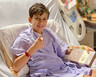 Nathaniel Clauss smiles while giving the thumbs up sign in a hospital bed while holding a box of chocolates