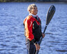 Vicki Reynolds stands in front of a lake holding her kayak padle