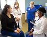 Three providers chat with a patient in a clinic room