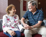 Sharon and Bill Conley hold hands while sitting on a couch