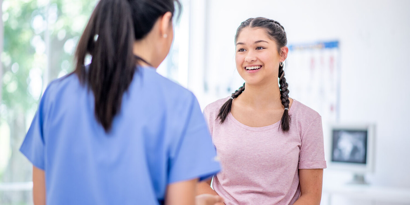 A provider speaks with a female teenage patient in an exam room
