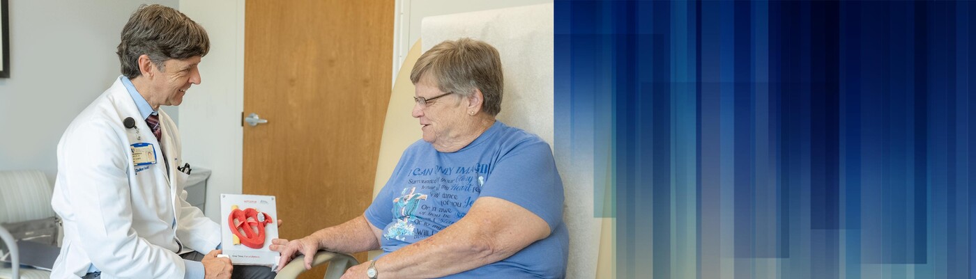 A doctor shows a patient a model of a WATCHMAN device in a clinic room