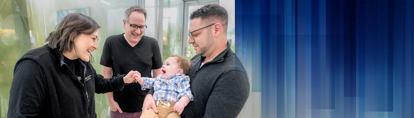 A provider and dad smile and play with a baby being held by his other dad.