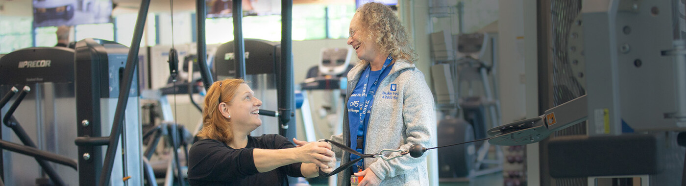 A trainer works with a client on a seated weight machine exercise