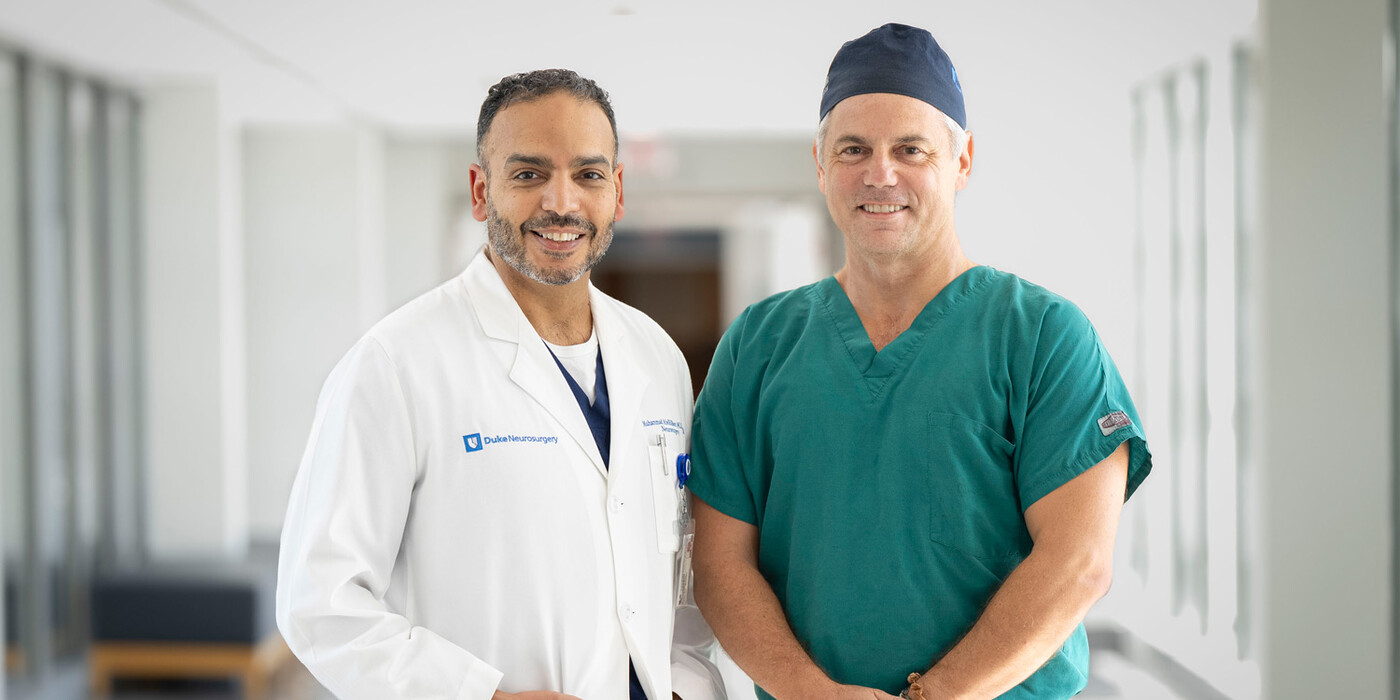 Two doctors stand, smiling at the camera in a hallway
