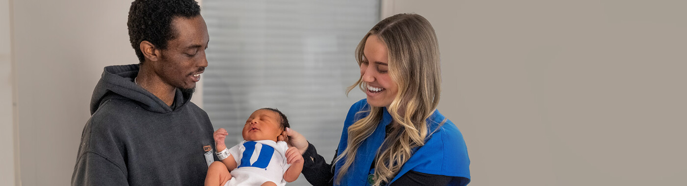 A nurse looks at newborn baby being held by its father.