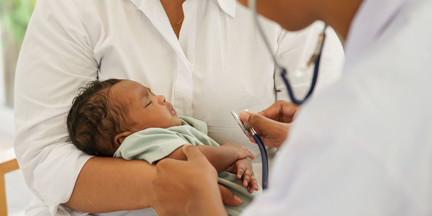 A parent holds a newborn baby while a doctor holds a stethoscope to it's chest