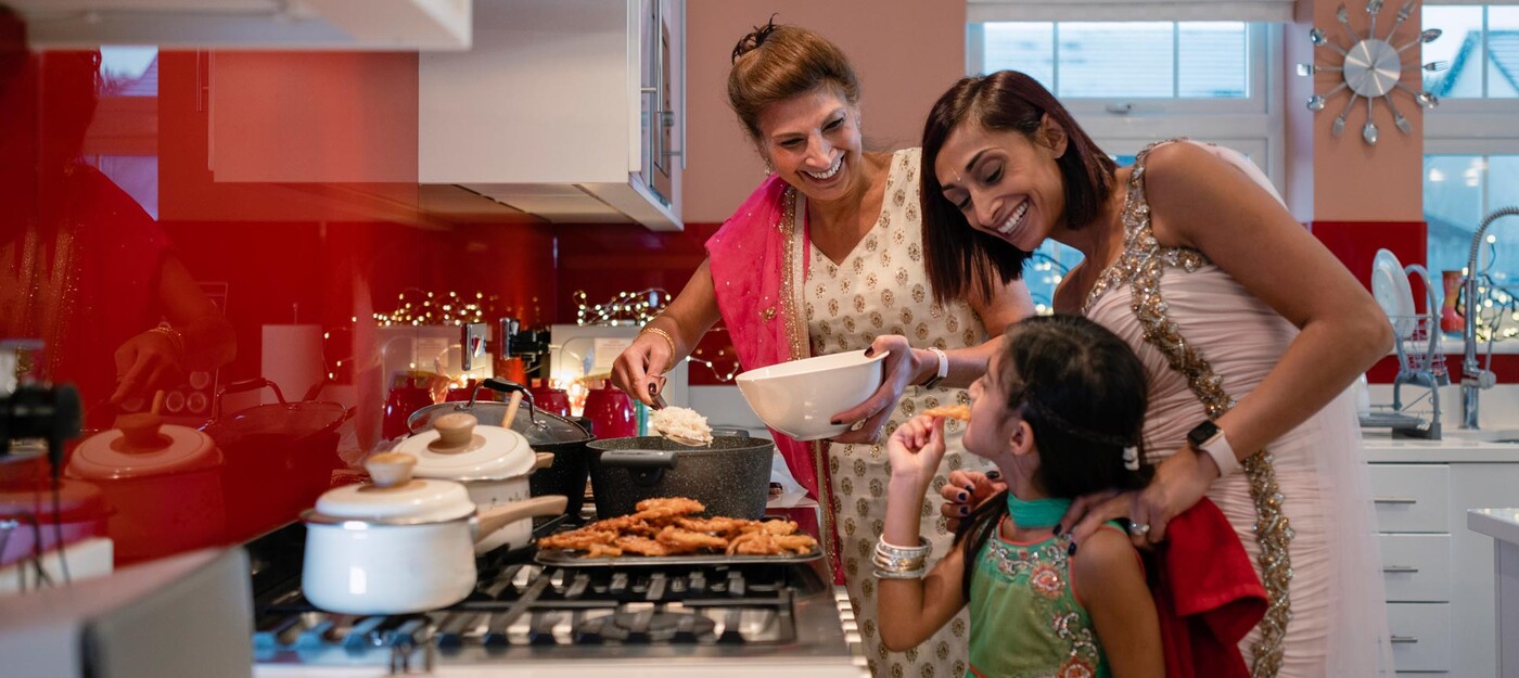 A grandmother, mother and girl cook and taste traditional Indian food together in the kitchen