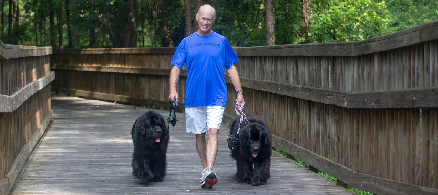 Kerry May walks with two large, black dogs on leashes.