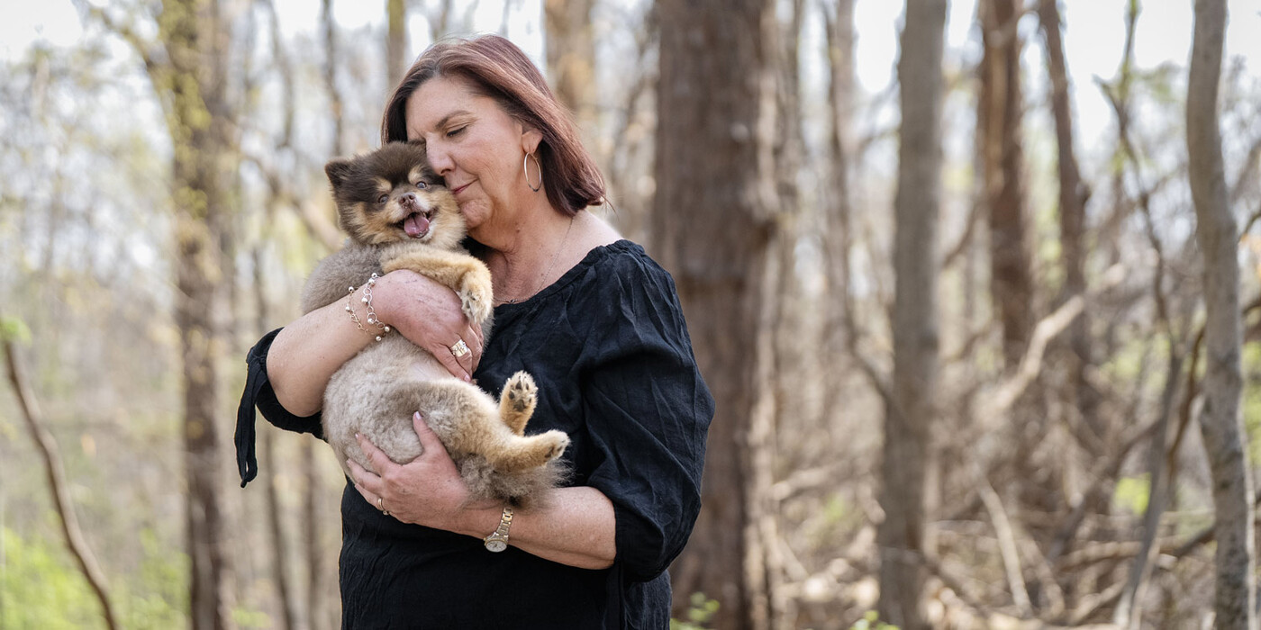 Juli stands on a forest trail and cuddles her dog Boba against her face