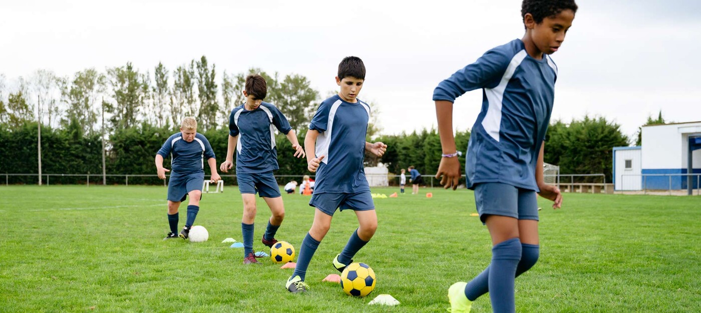 A youth boy's soccer team practices dribbling drills in a line around cones 