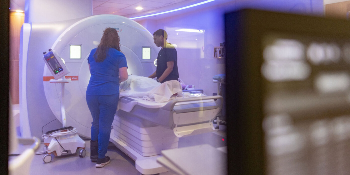 Two technicians help a patient get into an MRI machine