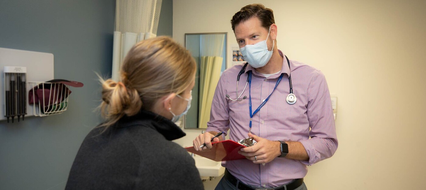 A provider holds a clipboard as he talks to a patient.