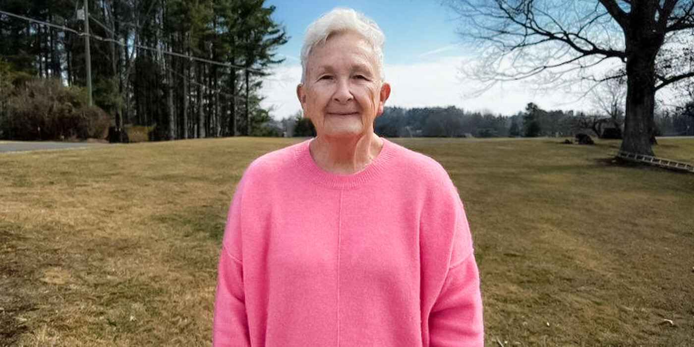 Sharon Davis stands outside. She is wearing a pink sweater.