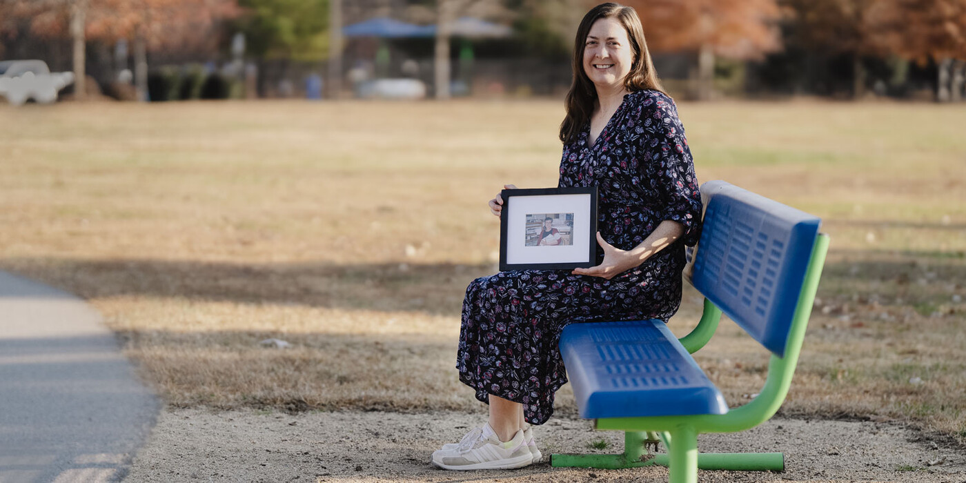 Kathryn Mathews sits on a bench and holds a photo of her mother