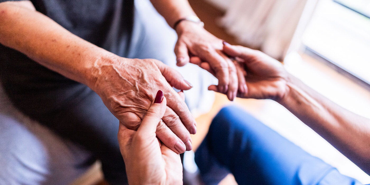 Un profesional de la atención médica sostiene las manos de un paciente anciano