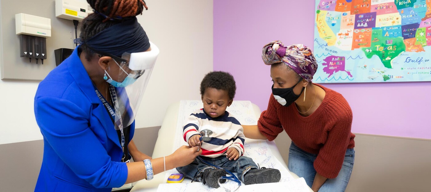 A provider shows a stethoscope to a young patient and his mother 