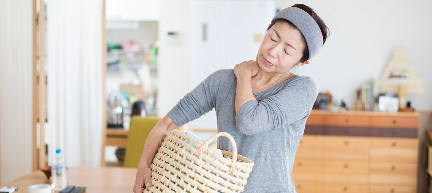 A woman holds her shoulder in pain as she carries a laundry basket