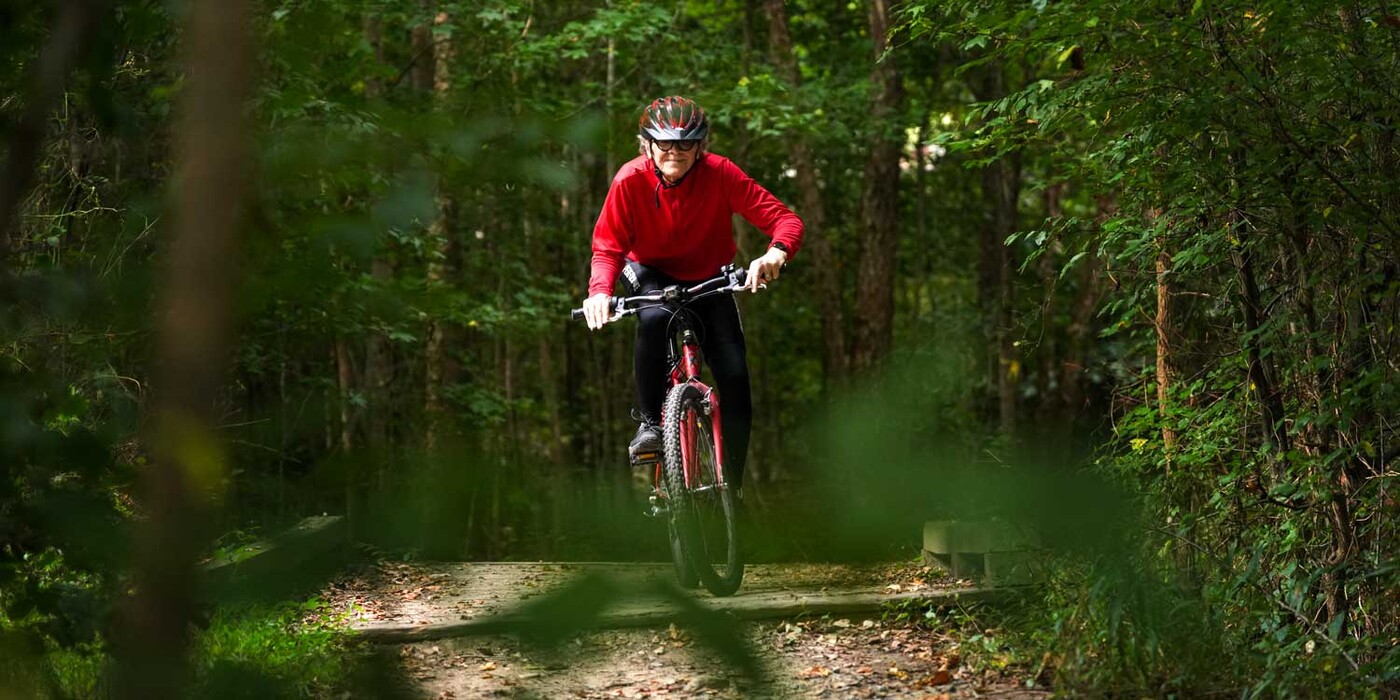 Steve Harlin rides his bike across a wooden bridge on a forested trail. 
