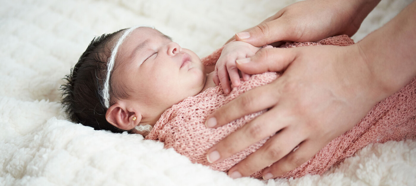 A mom's hands hold a baby on a blanket