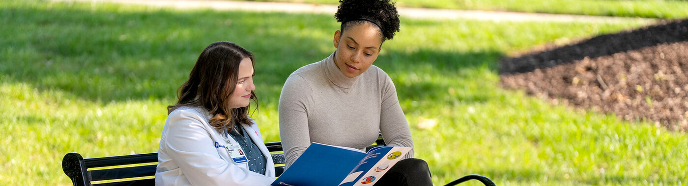 A doctor and patient go over some informational materials outside on a bench