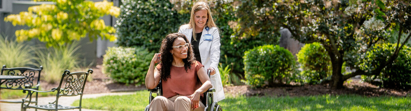 Un médico empuja a un paciente en silla de ruedas por un jardín