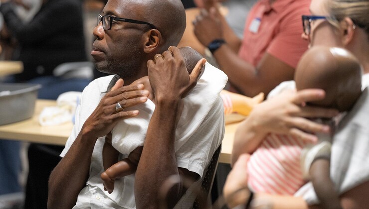 Los futuros padres practican los cuidados del recién nacido y habilidades de seguridad con muñecos durante una clase de preparación para la llegada del bebé.