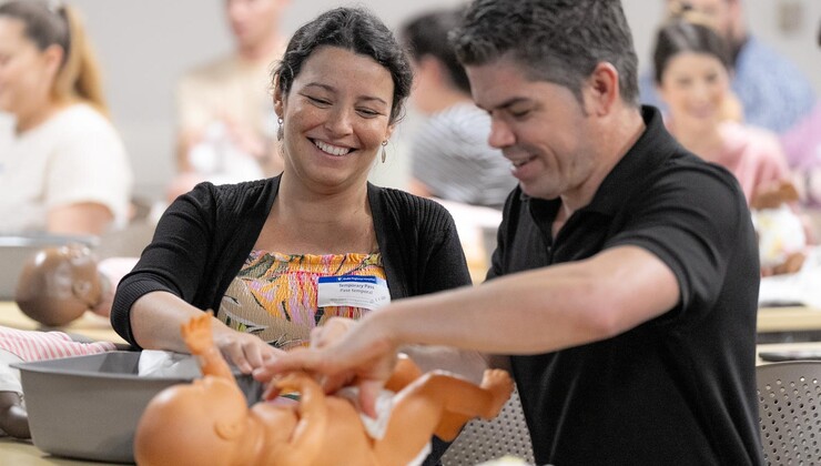 Los futuros padres practican con un muñeo cómo cambiar el pañal durante una clase de preparación para la llegada del bebé.
