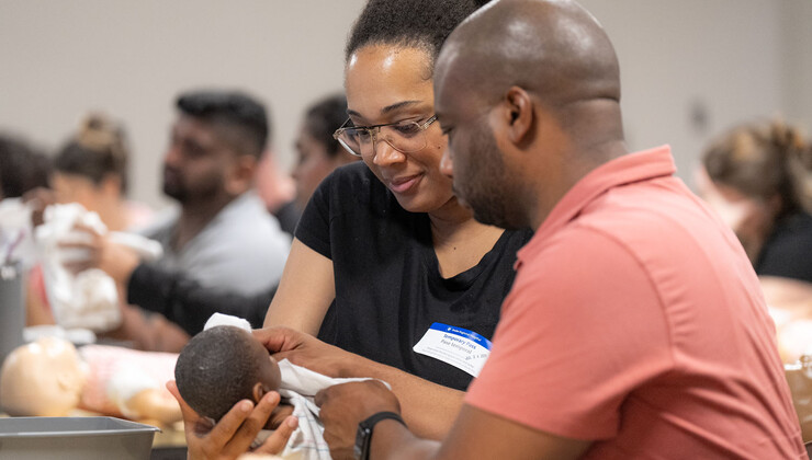 Una pareja practica técnicas de cuidado del recién nacido con un muñeco