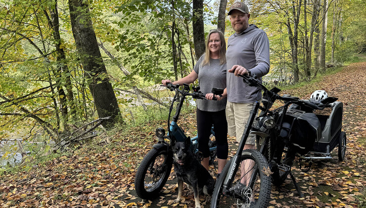 Dustin stands next to his wife Lisa on an outdoor trail with their bikes
