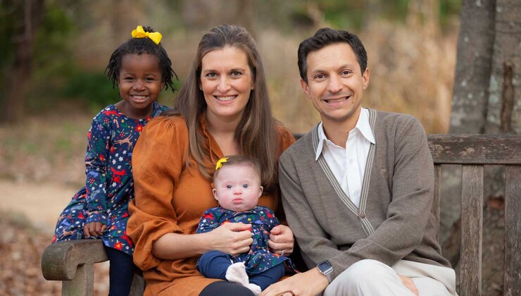 Izabel and her family smile outside on a bench 