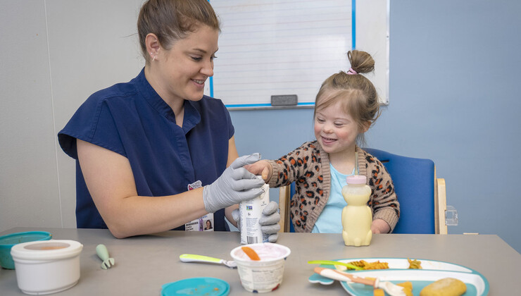 A therapist helps a pediatric patient with down syndrome close a bottle