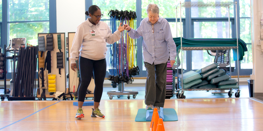 A trainer helps a woman walk across a balancing course at the gym